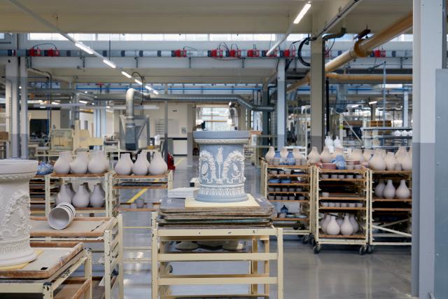 An image of the Wedgwood factory. In the center a Jasper wear piece sits on a factory trolley and behind you can see a busy factory filled with many varieties of pots.