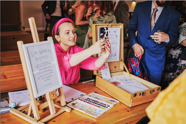Chloe Breeze on a table taking a picture of someone for a illustration