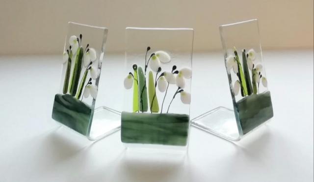 three glass ornaments with white snowdrop pattern and green leaves
