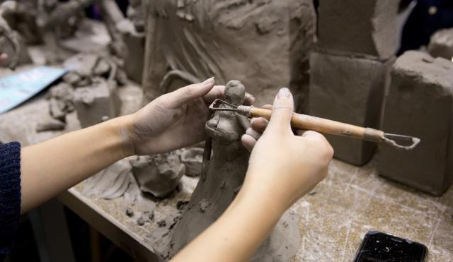 Hand using tool to create clay sculpture