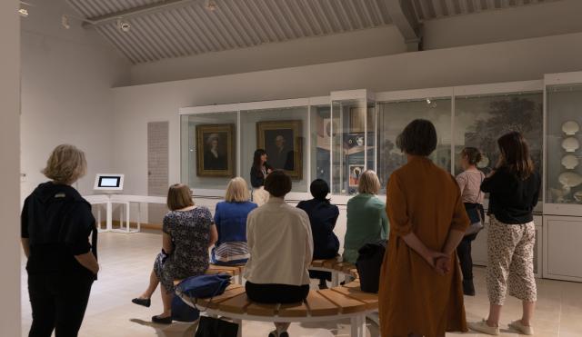 Group on a museum tour. Some people are sitting some are standing in the galleries