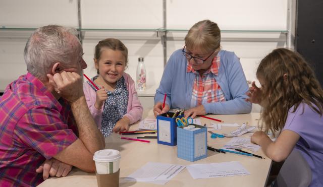 Family making puppets with a girl smiling with a pencil in hand