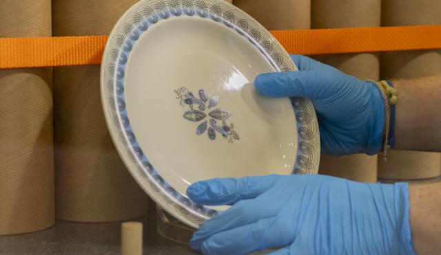 image of cwedgwood plate being handled by a person with blue gloves on. The plate has a blue pattern around the rim and in the centre