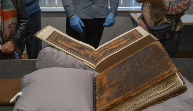 Image of book on grey cushions. The book is an old archive pattern book and brown in colour