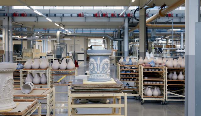 An image of the Wedgwood factory. In the center a Jasper wear piece sits on a factory trolley and behind you can see a busy factory filled with many varieties of pots.