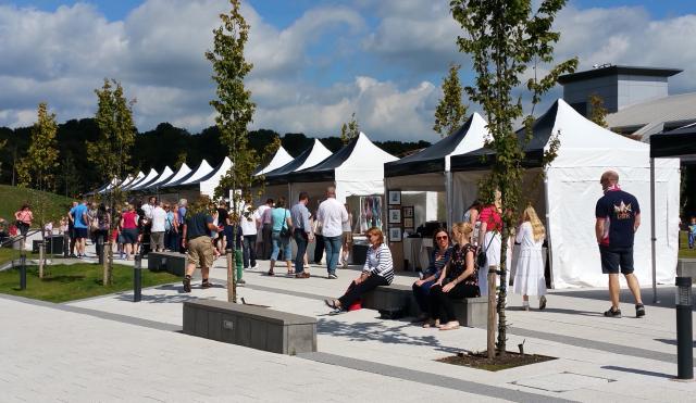 Market stalls lined up on the concourse with people in the picture leisurely browsing