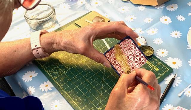 Image of a workshop table a lady holds a piece of ceramic in her hand and is brushing gold onto it